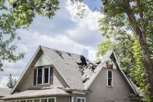 horizontal close up image of a roof of a house that has burned and fallen in under blue sky with cloud in summer time.