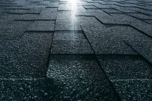 Soft roof tiled greenish grainy texture on the top of a modern building; green soft roofing tiles covering a dacha house lit by the sun with the flare; wide-angle view