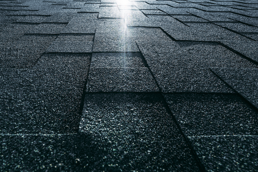 Soft roof tiled greenish grainy texture on the top of a modern building; green soft roofing tiles covering a dacha house lit by the sun with the flare; wide-angle view