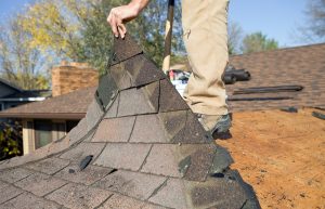a man peeling off curled singles from his roof