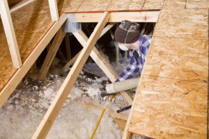 A picture of a man in a small attic space putting in blown in attic insulation